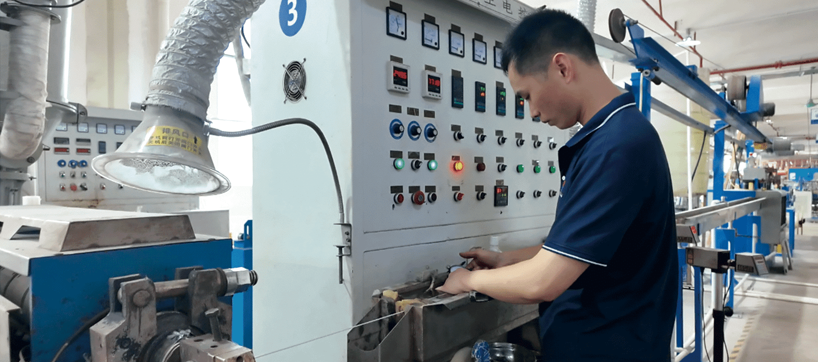 HULK manufacturing facility showing a skilled technician operating a cable extrusion machine control panel; the worker is precisely adjusting settings amidst complex instrumentation and indicator lights, ensuring optimal insulation thickness and material consistency during the high-temperature extrusion process.