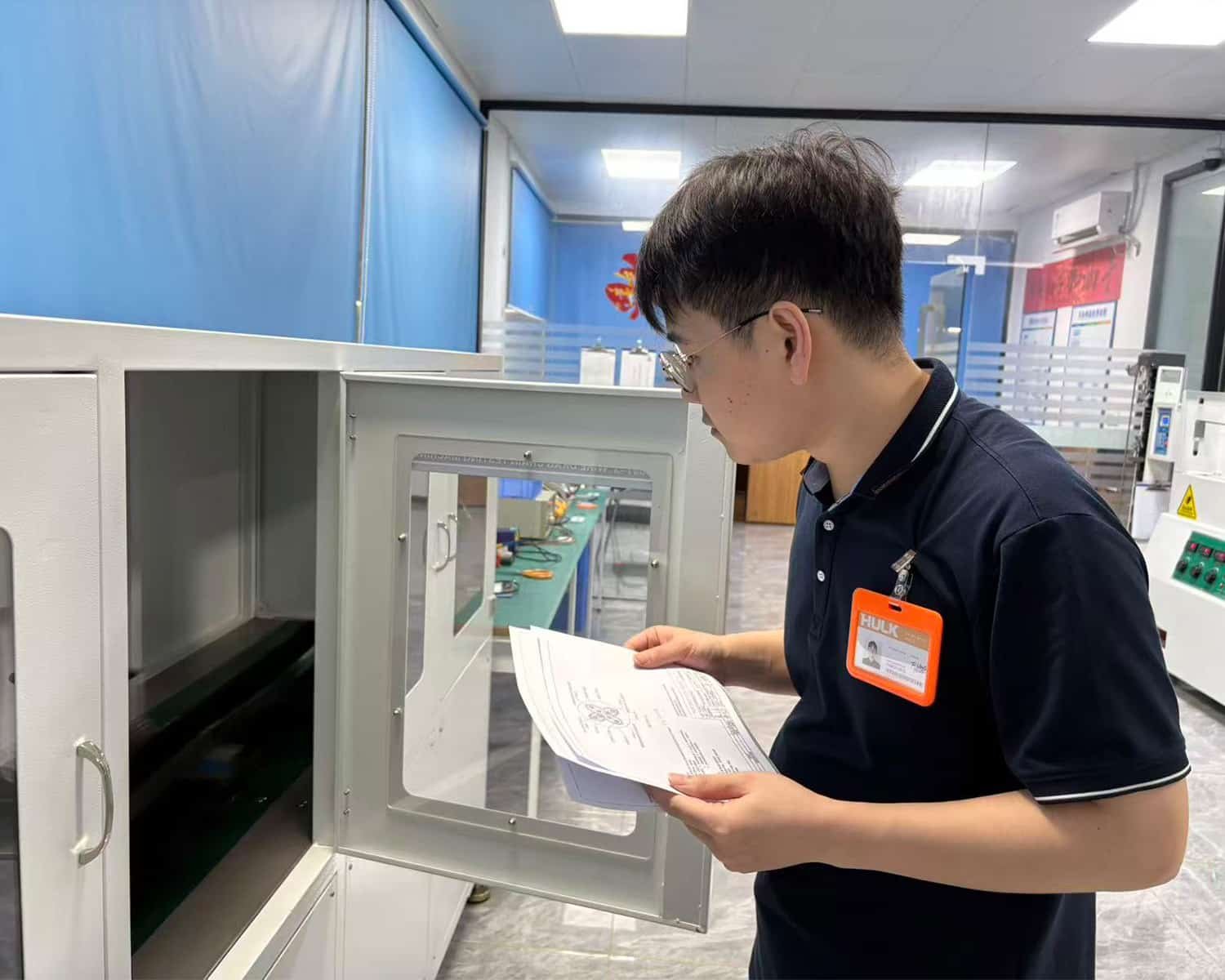 HULK quality engineer reviewing technical specifications against a test chamber in the R&D lab; verifying environmental durability and compliance of cable samples to ensure every batch meets rigorous international standards before delivery.