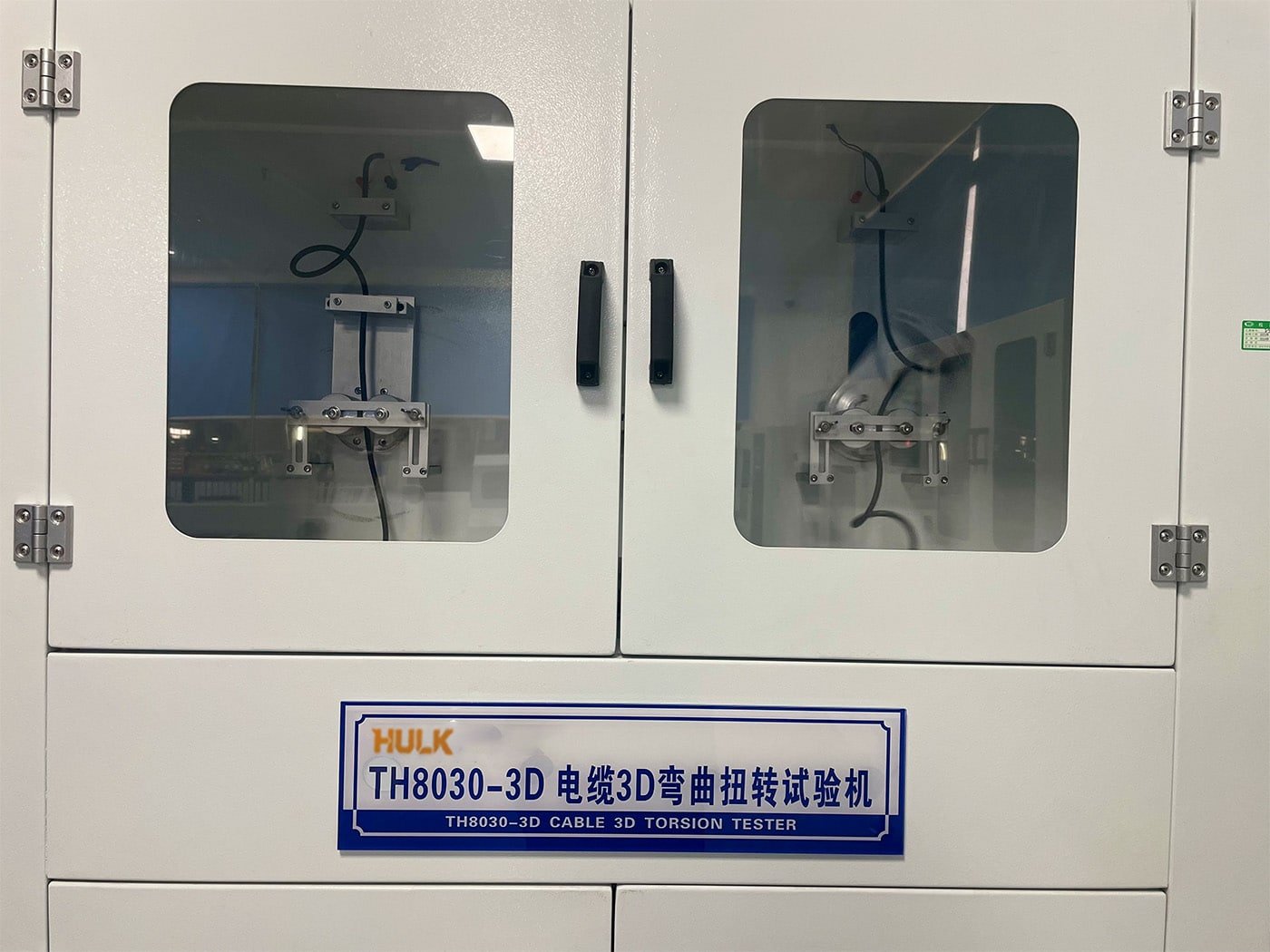The HULK TH8030-3D Cable 3D Torsion Tester in operation, visible through the safety glass enclosure; this specialized laboratory equipment simulates complex multi-axis bending and twisting motions to rigorously validate the fatigue resistance and lifespan of HULK high-flex cables before mass production.