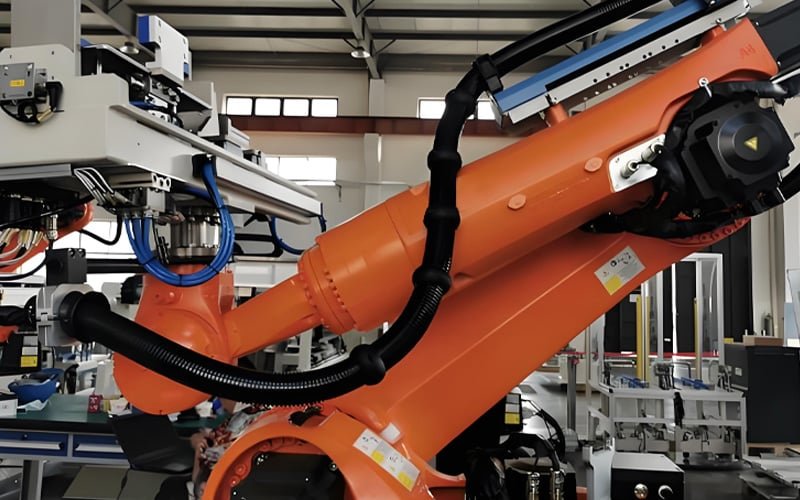 HULK cables housed in black corrugated conduit along the joints and arm of a large orange industrial robot, engineered for dynamic motion, physical protection, and long-term durability in high-stress manufacturing environments.