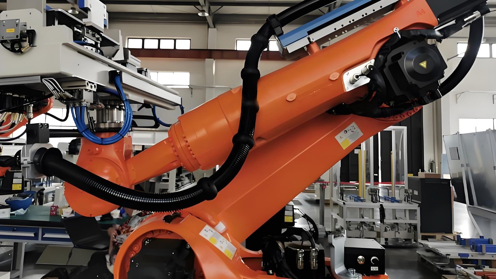 A close-up of an orange heavy-duty industrial robotic arm in a factory setting, featuring HULK black corrugated pipeline bundles integrated along its joints; the bundles demonstrate extreme flexibility and durability while enduring complex multi-axis movements, highlighting their suitability for advanced automation and robotics applications.