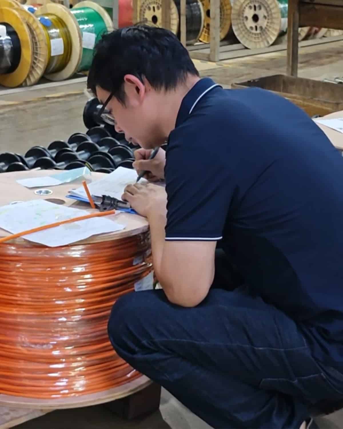 HULK technician conducting rigorous incoming quality control on a large orange cable reel, verifying conductor dimensions and material specifications at the production source to ensure premium quality.