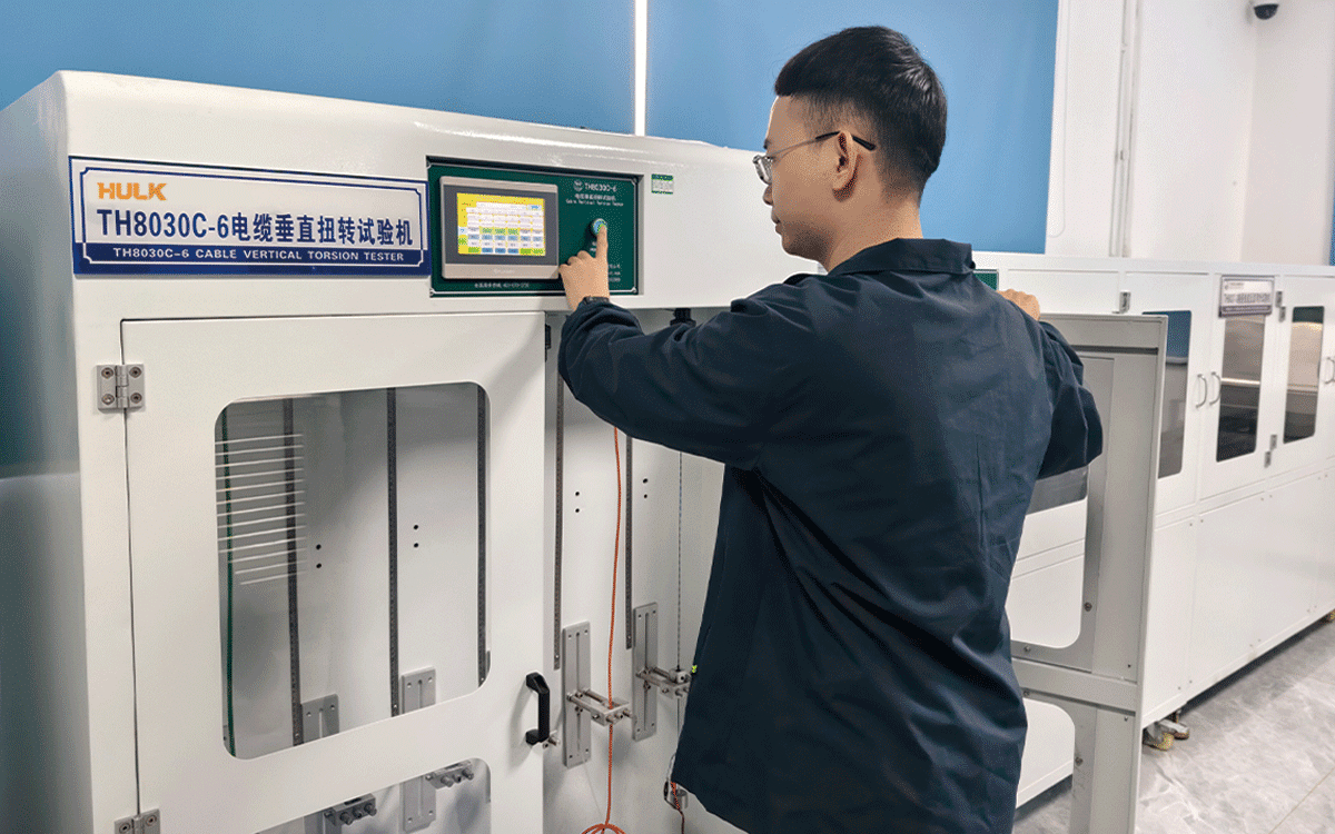 Engineer operating a HULK TH8030C-6 Cable Vertical Torsion Tester in a lab setting; the white machine with a green touchscreen interface is used to apply controlled vertical twisting forces to cable samples, validating their resistance to torsional stress and structural integrity under dynamic installation or operational conditions.