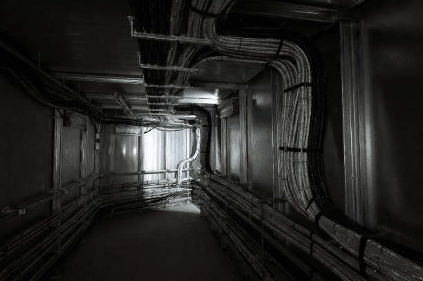 Bundled low smoke zero halogen cables running along walls in a dimly lit enclosed industrial tunnel or equipment corridor, highlighting safe installation for limited ventilation and evacuation safety in industrial facilities