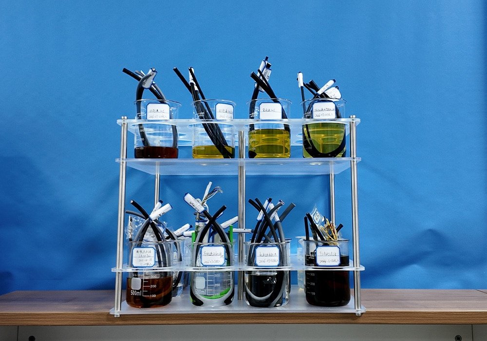 Hulk Cable chemical resistance testing scene showing multiple cable samples submerged in beakers containing various industrial oils and solvents on an acrylic rack, validating jacket durability against chemical corrosion and swelling