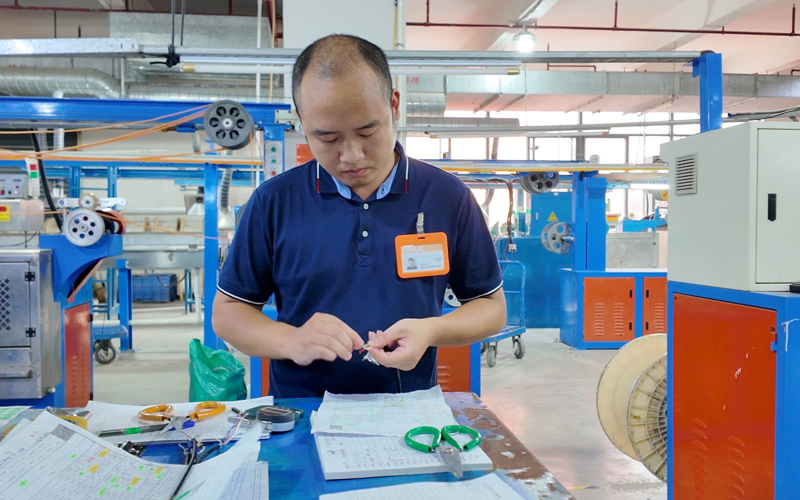 Hulk Cable technician dissecting a cable sample at the production workstation to inspect internal conductor structure and insulation quality, with calipers and inspection logs on the table, ensuring manufacturing compliance