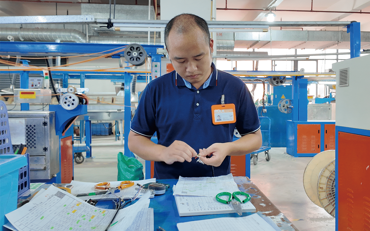 Hulk Cable material evaluation lab with technician testing PVC, TPU, TPE, silicone and halogen-free samples using precision tools on blue workbench in factory setting