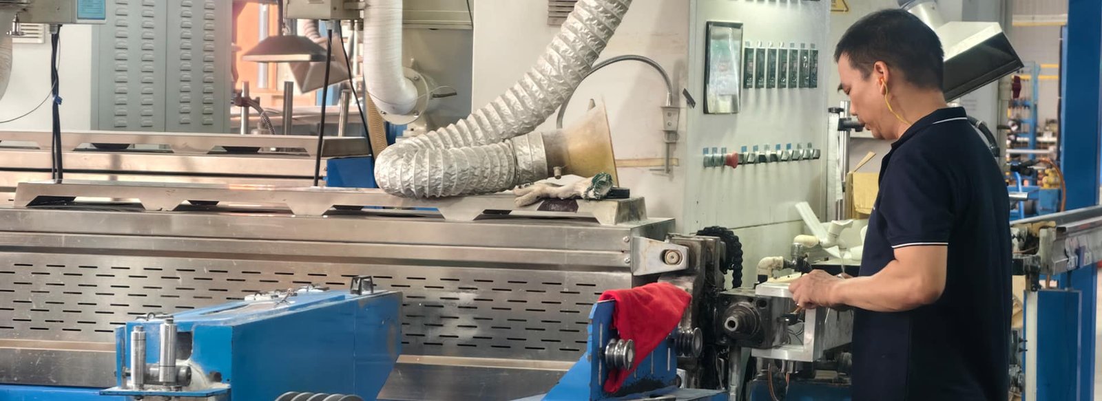 Hulk Cable manufacturing workshop scene showing a technician operating a large blue cable extrusion machine, monitoring the precision molding of cable jackets with industrial ventilation and control systems in the background