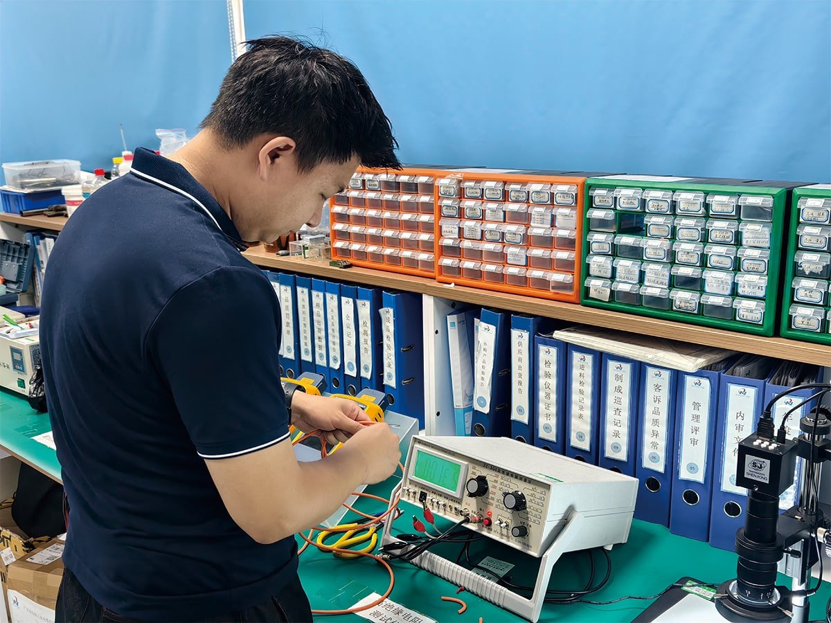 Hulk Cable quality control laboratory scene showing a technician performing precise resistance testing on cable samples using digital equipment, with organized component bins and blue inspection record binders in the background ensuring traceability and ISO-standard compliance