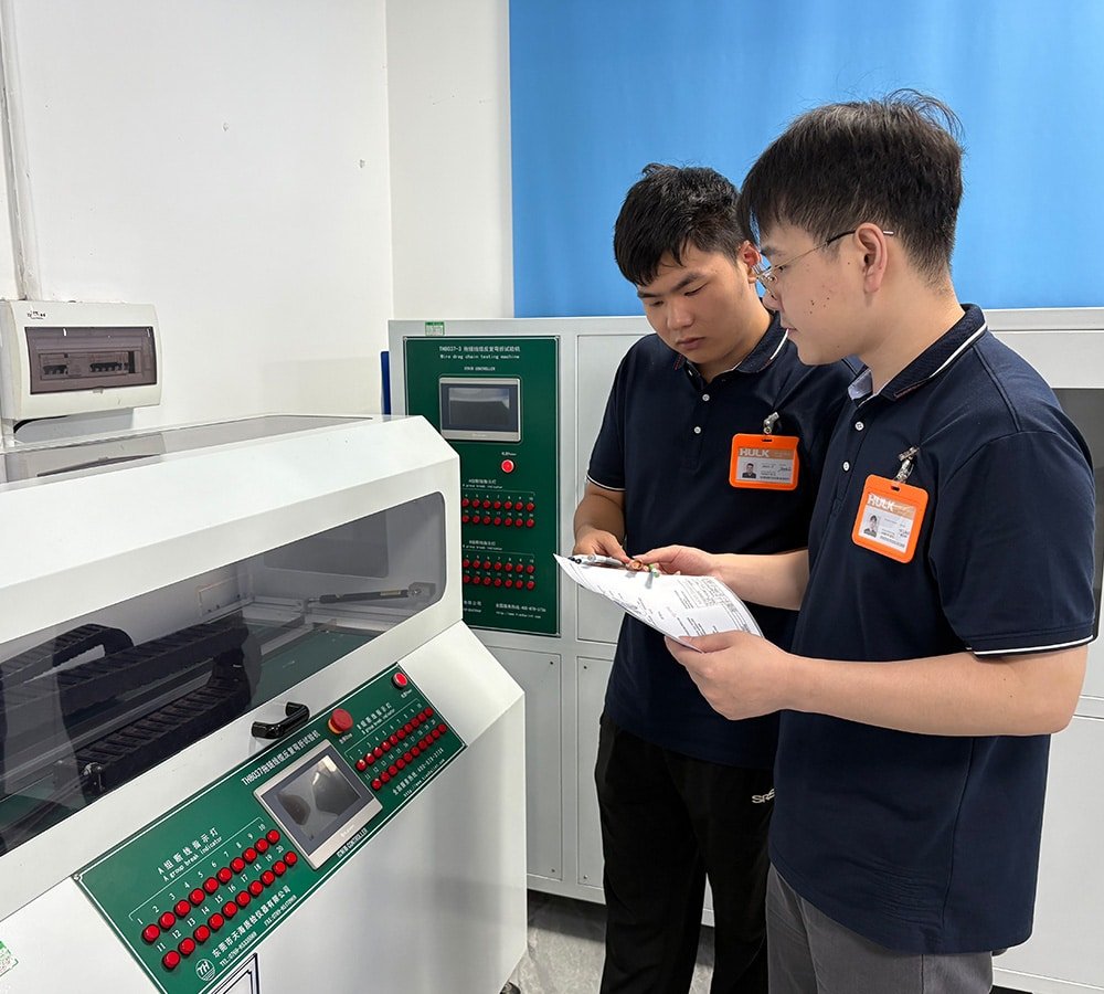 Hulk Cable engineers conducting quality testing in a lab, using TMR027 and TMR022-3 cable flex life testers to record data on drag chain and servo motor cable durability, emphasizing precision and traceability in product validation