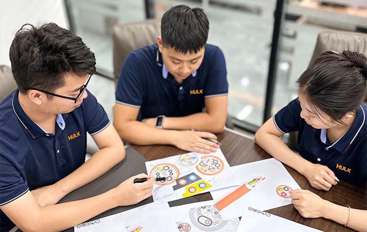 Three Hulk Cable engineers reviewing cable cross-section diagrams and color-coded wiring plans at a meeting table, demonstrating collaborative R&D for customized industrial cable solutions