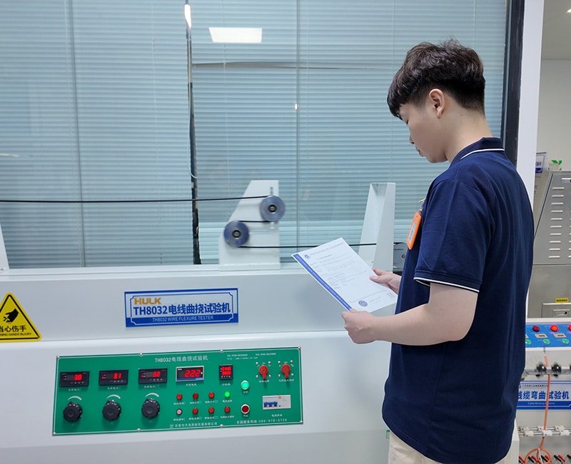 Hulk Cable technician reviewing test report beside TH8032 Wire Flexure Tester, conducting high-cycle bending durability tests to validate mechanical lifespan and signal integrity of flexible industrial cables