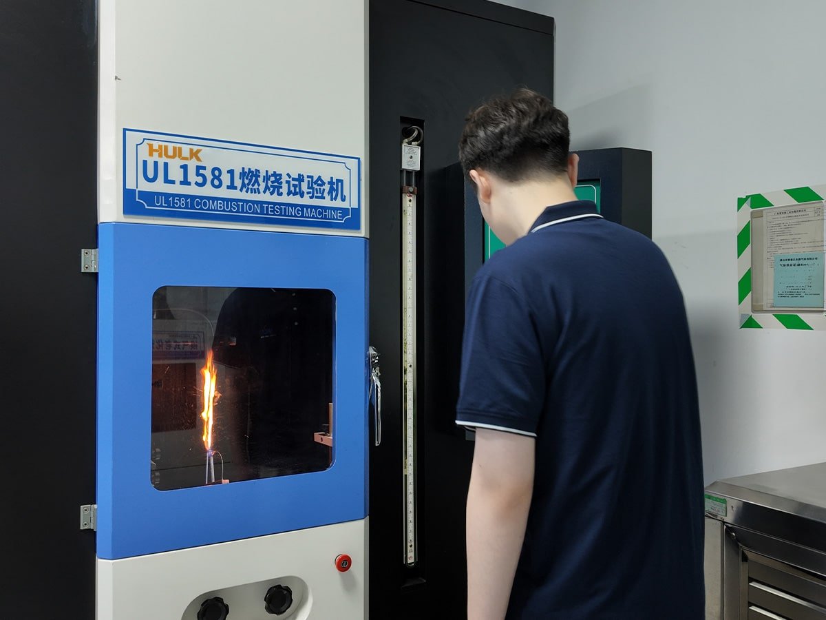 Hulk Cable UL1581 combustion testing machine in laboratory, with technician observing flame test on cable sample to verify flame retardancy and smoke density compliance for industrial and rail transit safety standards