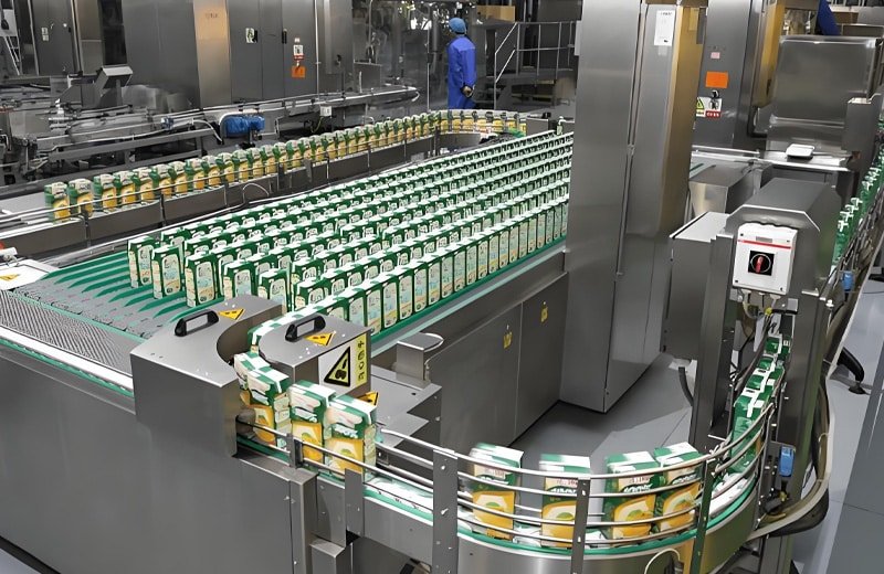 Hulk Cable application in dairy or liquid food packaging line showing green-and-yellow cartons moving on stainless steel conveyor with multiple curves and diverters, highlighting cable flexibility and resistance to moisture and chemicals