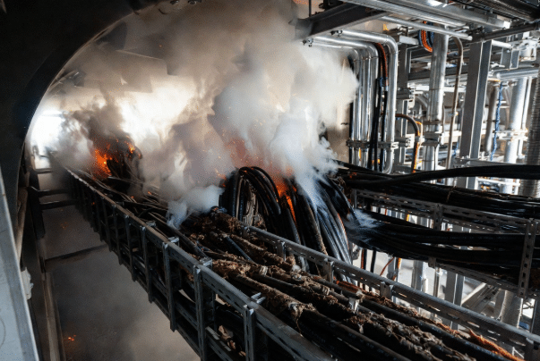 Realistic view of bundled halogen-containing PVC cables in industrial cable tray during fire event with dense smoke and glowing insulation, contrasting safety challenges addressed by LSZH designs in food processing, automation and infrastructure applications